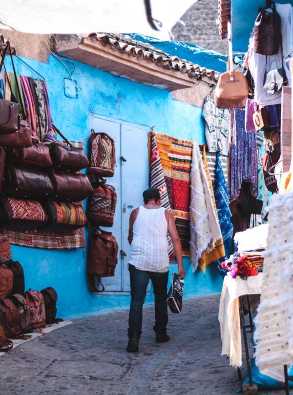 Explore the lively market alley filled with textiles and bags in Chefchaouen, Morocco travel ,12 days tour from Casablanca