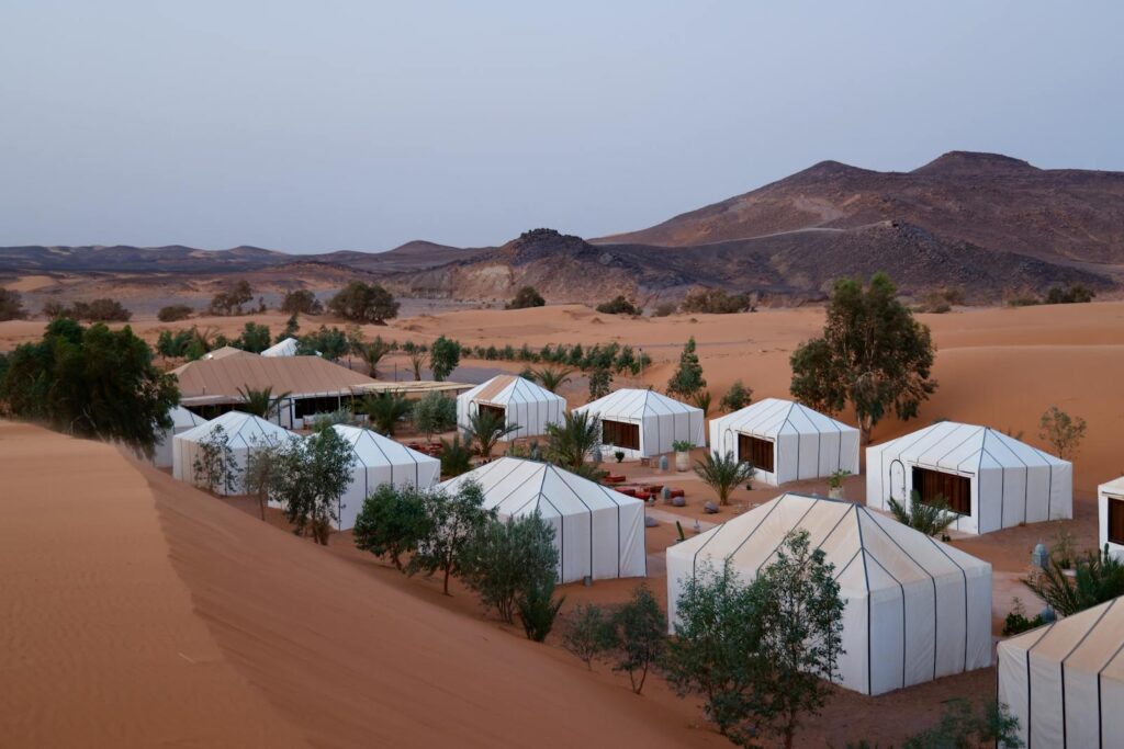 Aerial view of luxury tents in desert landscape with hilly background and twilight ambiance.Morocco travel ,Best 7-Day Morocco Trip from Marrakech