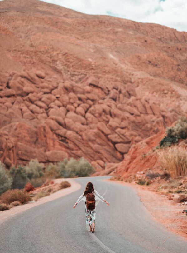 A person with a backpack walks on a winding road in Morocco's mountainous desert landscape. morocco travel 10 days tour from marrakech