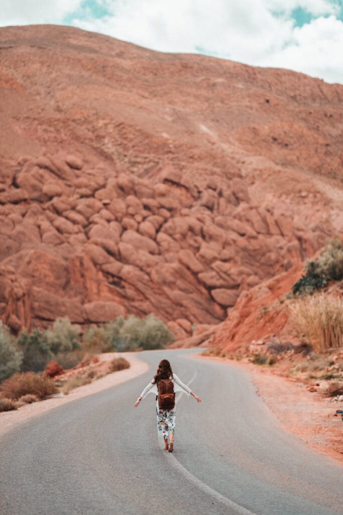 A person with a backpack walks on a winding road in Morocco's mountainous desert landscape. morocco travel 10 days tour from marrakech